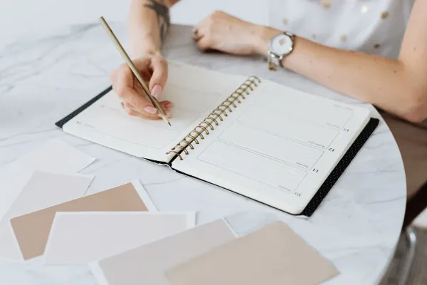 A hand writing in an open planner on a white marble table